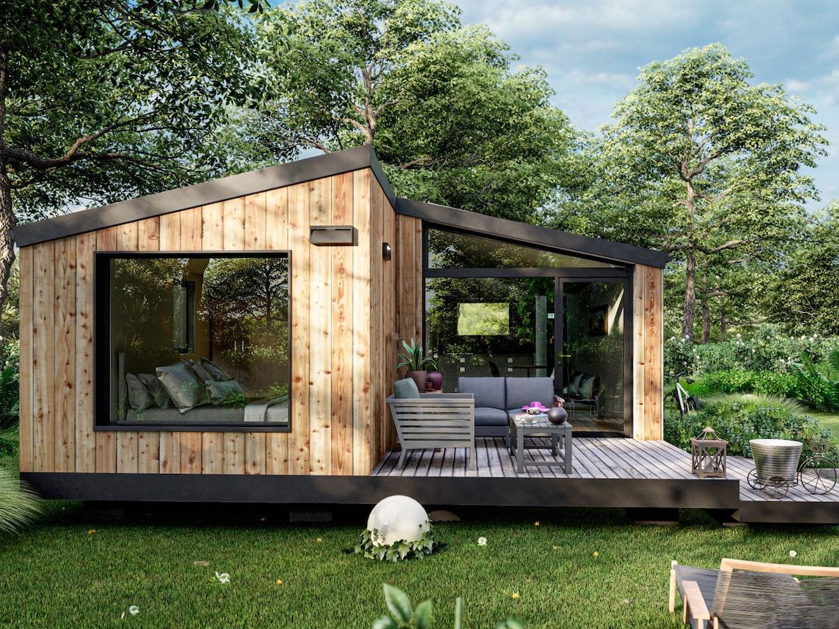 Modern tiny house with wooden exterior and large windows surrounded by lush greenery and trees.