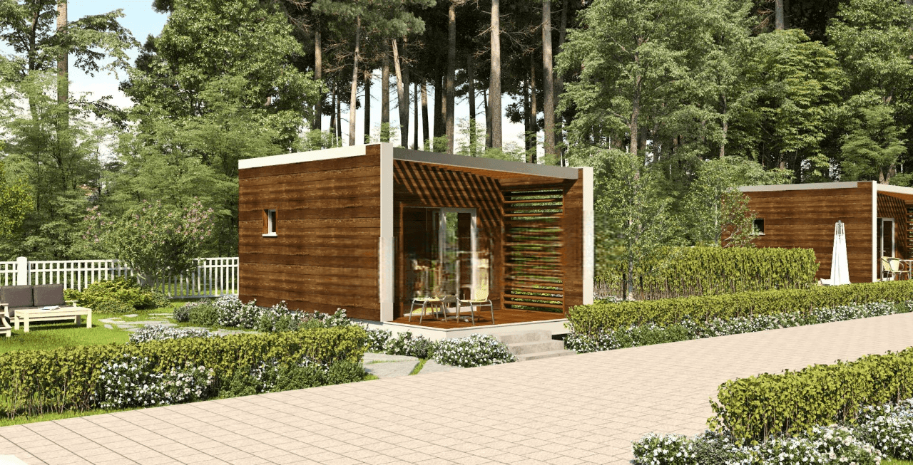 Modern wooden cabins in a forest setting with lush greenery and a paved walkway.