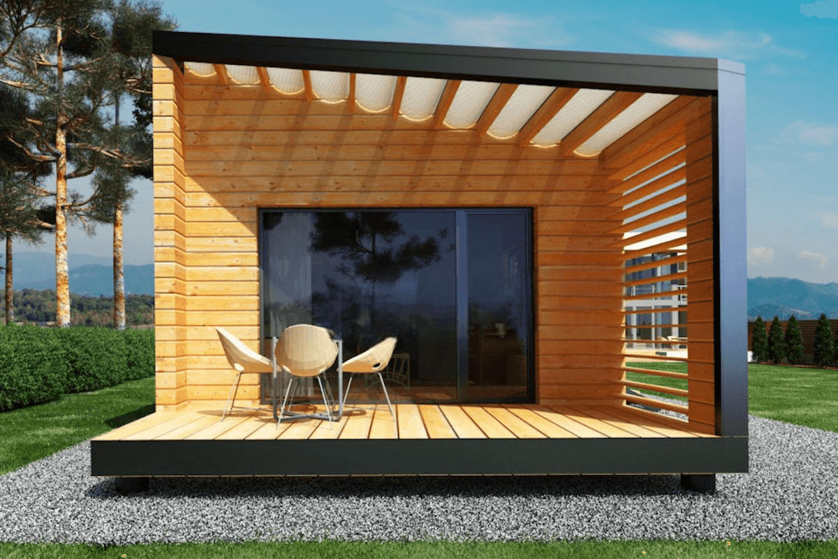 Modern wooden cabin with glass door and deck, surrounded by trees and grass.