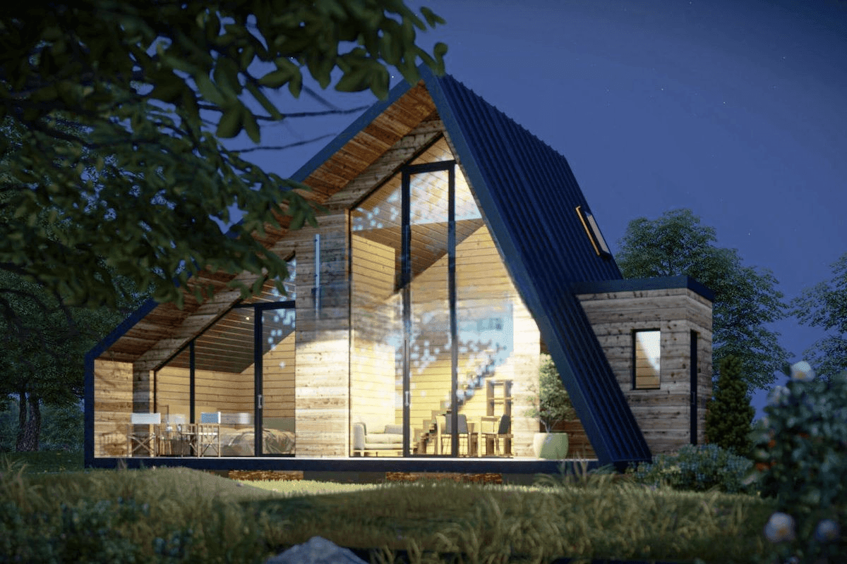 Modern A-frame cabin with large windows illuminated at night, surrounded by trees and grass.