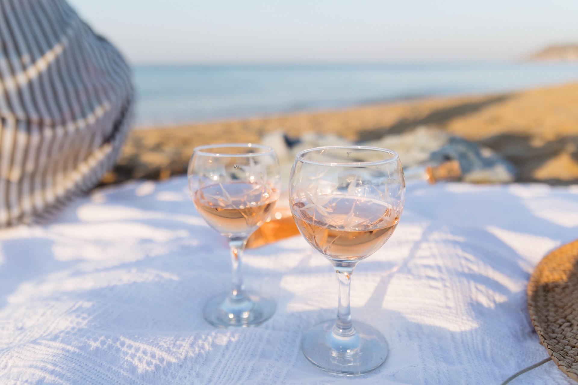 Pique-nique d’été sur la plage au coucher du soleil. Jeune femme avec un verre de vin rose. Pique-nique du week-end. Gros plan.